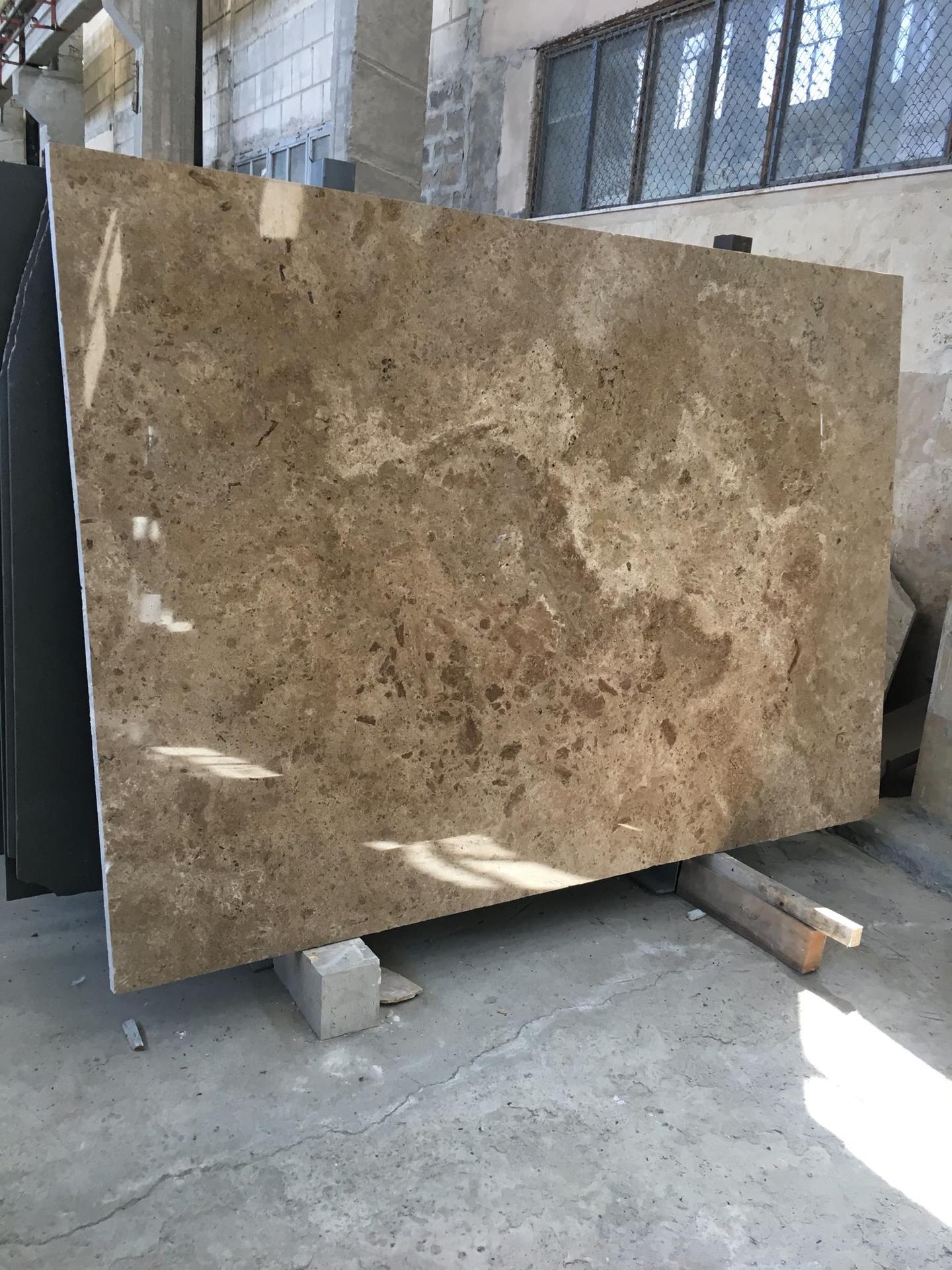 Polished cross-cut travertine slab standing in the workshop